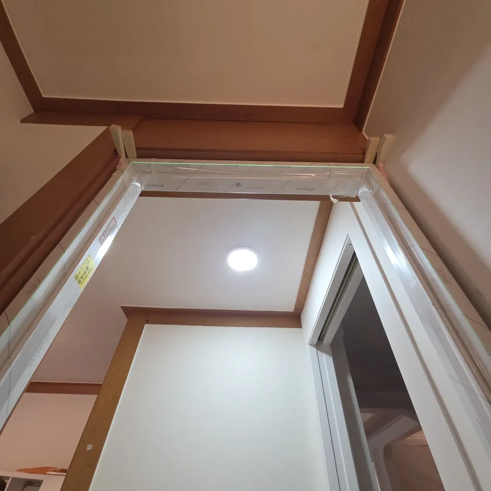 화성 몰딩교체 문 위 모서리에서 갈색 천장몰딩과 흰 문선이 만나는 이음부